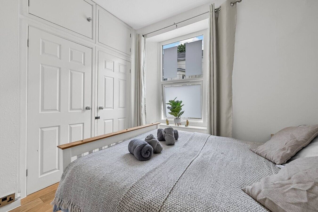 Un dormitorio con una cama grande, una ventana con cortinas, una planta en el alféizar y un armario.