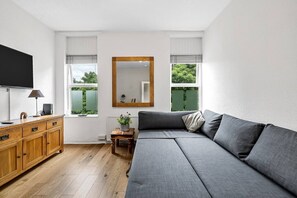 Ein modernes Wohnzimmer mit grauem Sofa, Holzschrank und Flachbildfernseher.