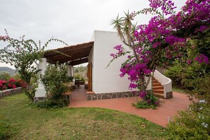 A covered outdoor area with a stone wall, a wooden pergola, and a staircase leading to a white building. - Olivetta – Vacation Home with Ocean View & Garden, Lipari (Aeolian Islands) (Lipari)