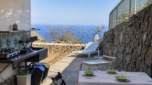 Une terrasse extérieure équipée d’un barbecue, d’une table à manger, de chaises et offrant une vue sur la mer.