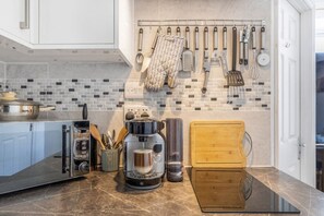 A kitchen with a coffee maker, a cutting board, and various utensils hanging on the wall. - Lovely spacious, quiet ground floor apartment (Plymouth)