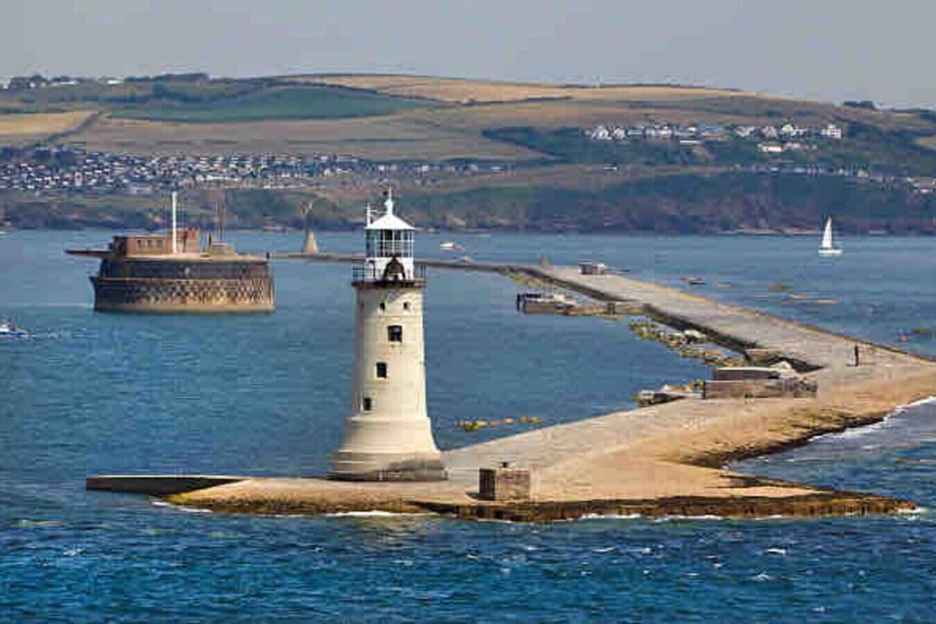 A lighthouse on a small island with a pier extending into the water, surrounded by calm sea and distant hills.