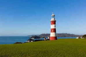 Un phare doté d’une tour rayée de rouge et de blanc, avec un premier plan verdoyant et une étendue d’eau en arrière-plan.