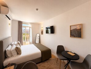 Ein Hotelzimmer mit Bett, Fernseher, Schreibtisch mit Stühlen und einem Fenster mit Vorhängen.