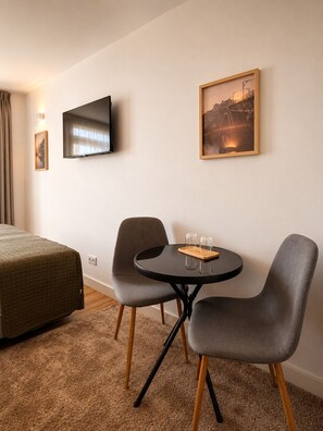 Ein Hotelzimmer mit einem Bett, einem Fernseher, einem gerahmten Bild, einem kleinen runden Tisch mit Gläsern und zwei Stühlen.