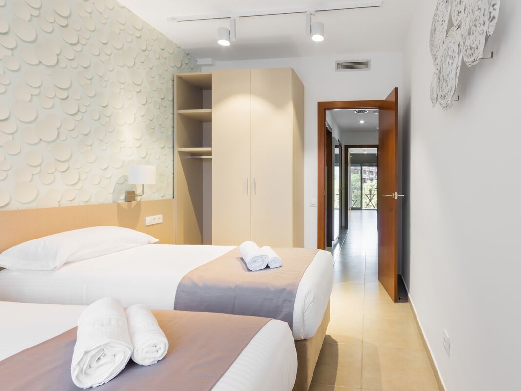 A hotel room with two beds, a wardrobe, a lamp, and a view through an open door.