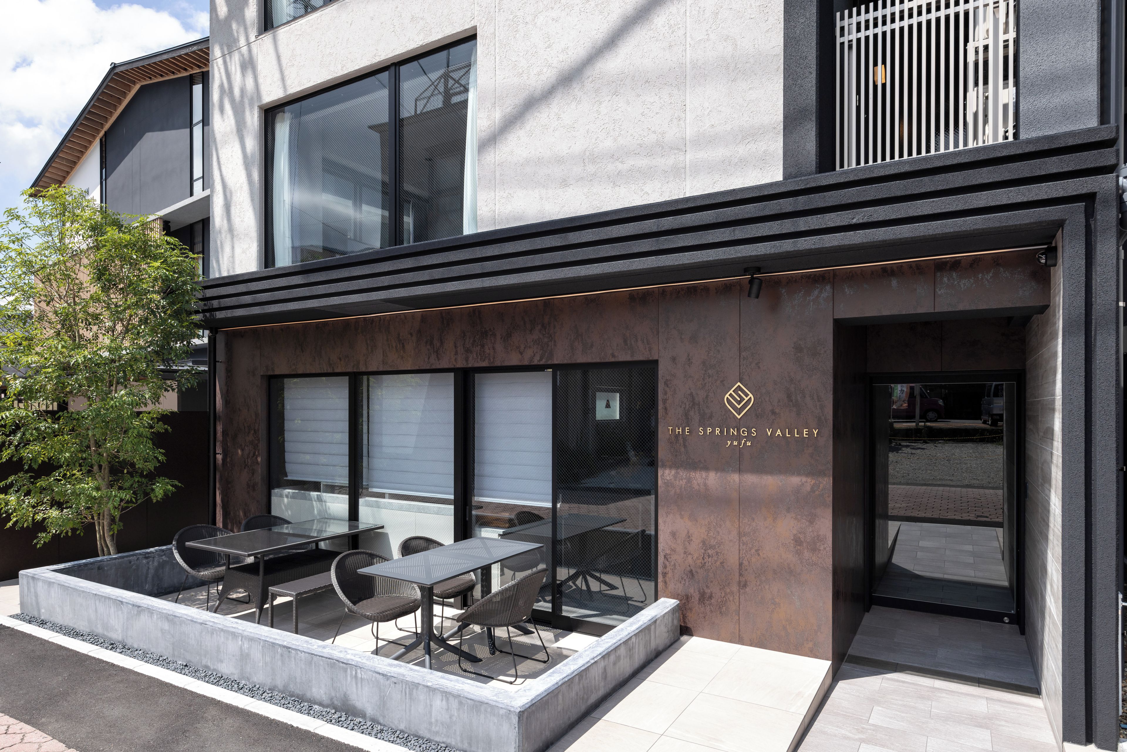 A modern building with a glass facade, outdoor seating area, and a sign reading 'THE SPRING VALLEY'.