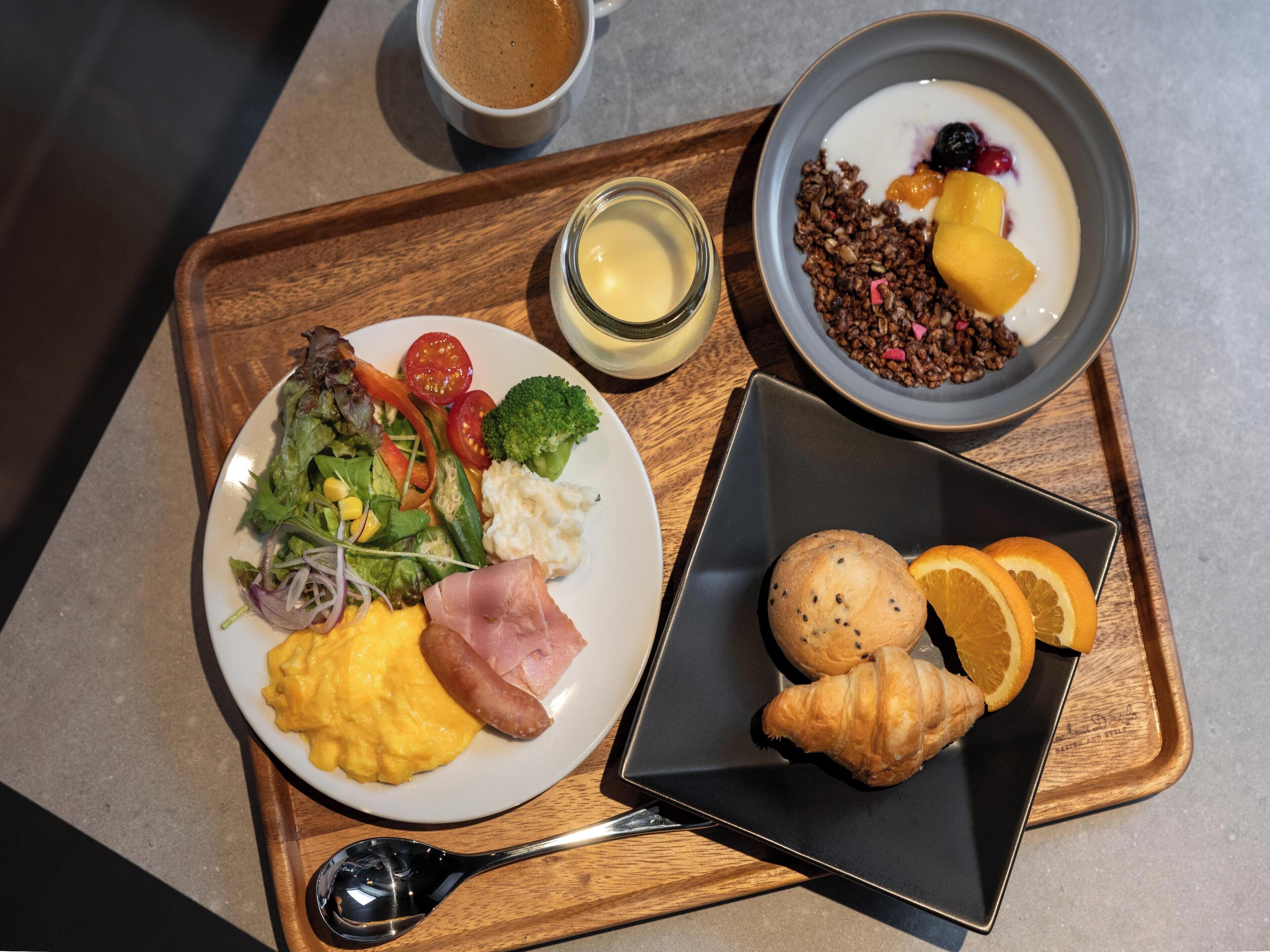 Una bandeja con alimentos para el desayuno, incluyendo huevos revueltos, jamón, ensalada y un croissant.