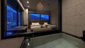 A modern hotel room with a large bed, a glass-enclosed jacuzzi, and a city view.