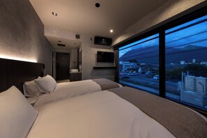 Habitación de hotel con una cama grande, un escritorio y vistas a un paisaje urbano a través de un ventanal.