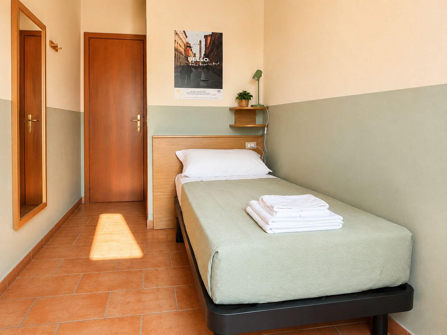 Un dormitorio con cama, mesita de noche, estante en la pared con una planta y un cartel.