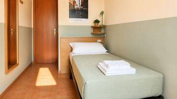 Un dormitorio con cama, mesita de noche, estante en la pared con una planta y un cartel.
