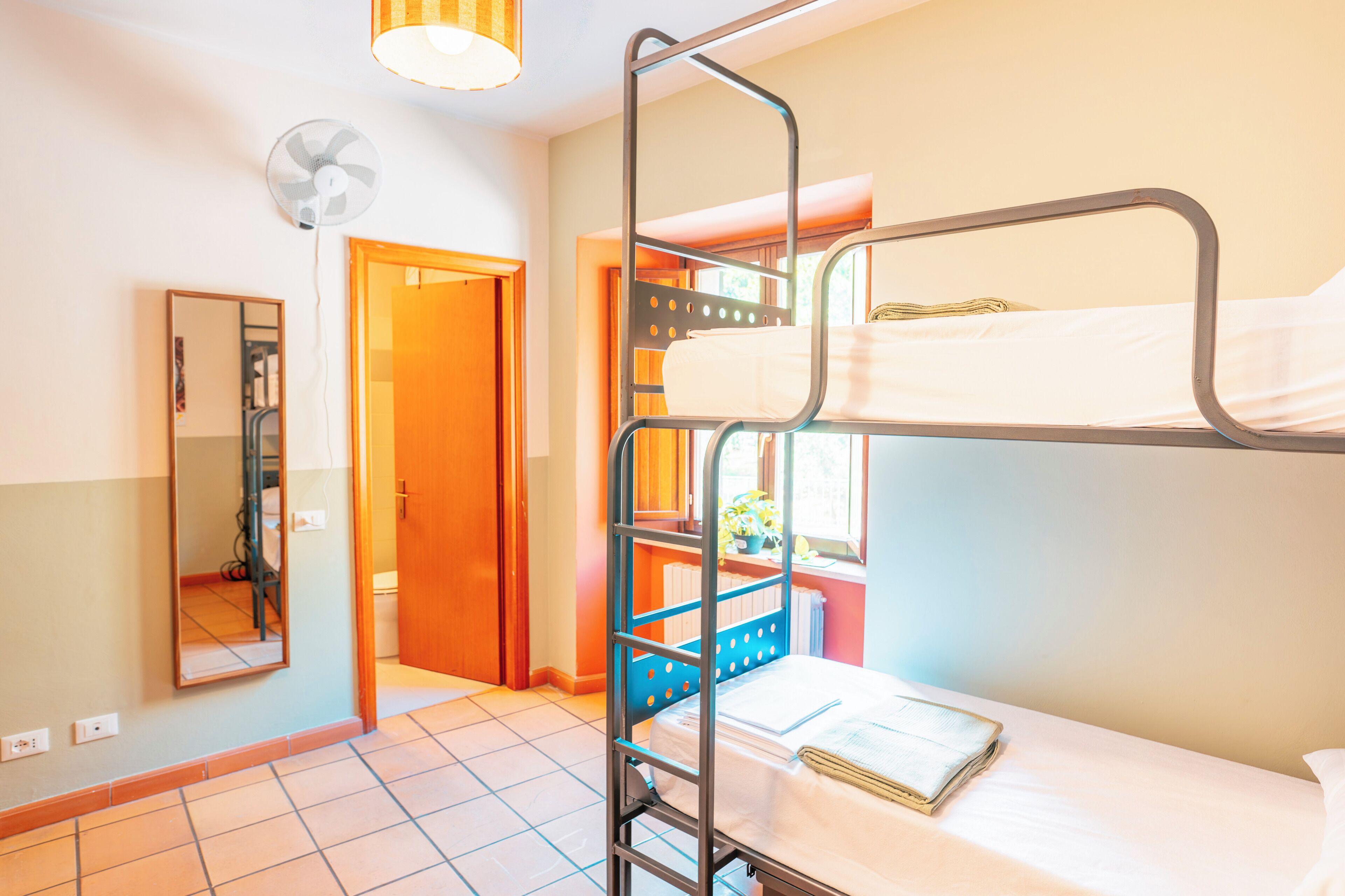 Ein Schlafsaalzimmer mit Etagenbetten, einem Spiegel, einem Ventilator und einem Fenster mit Blick.