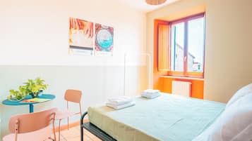 Habitación de hotel con cama, una silla, una mesita con una planta y una ventana con vista a edificios.