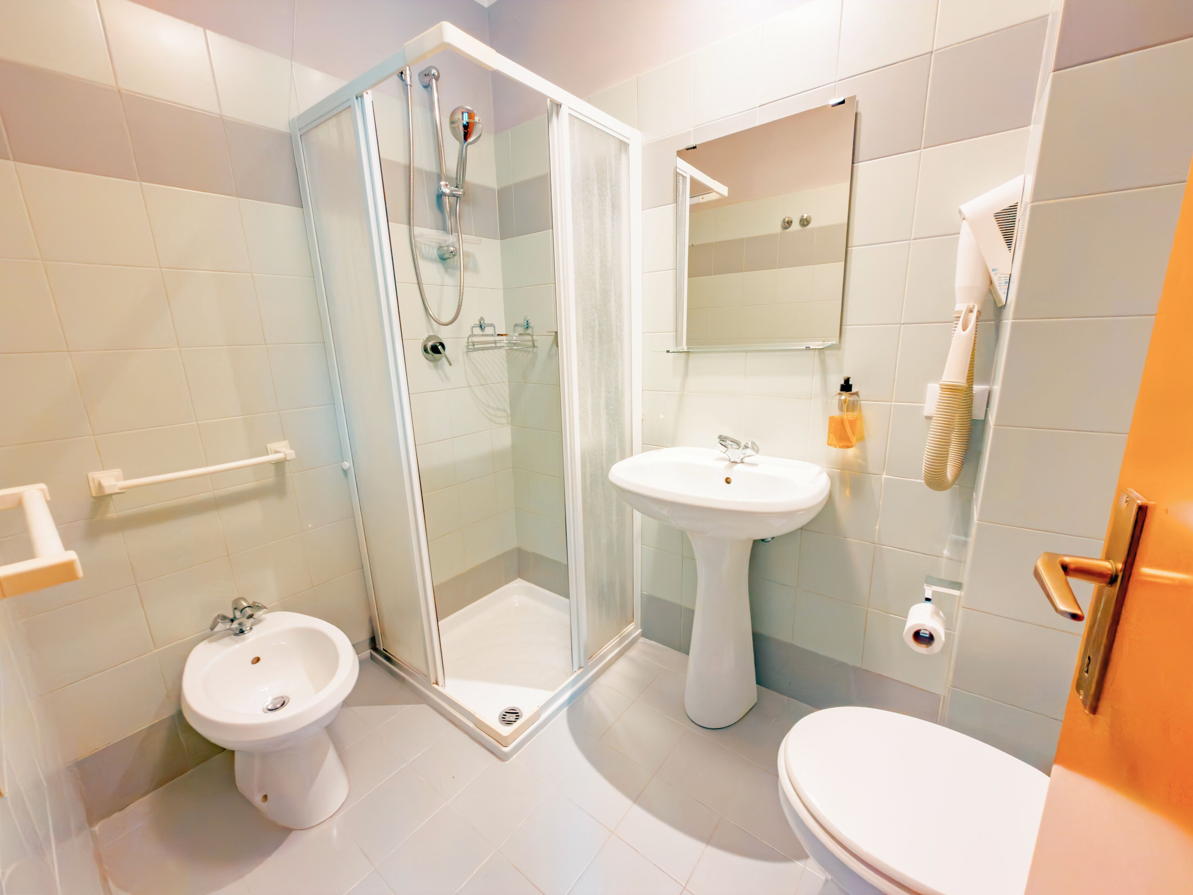 Ein Badezimmer mit Duschkabine, einem Waschbecken auf Säule, einer Toilette und einem Spiegel über dem Waschbecken.