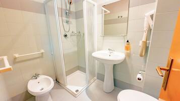 Een badkamer met een douchecabine van glas, een wastafel op voet, een toilet en een spiegel boven de wastafel.