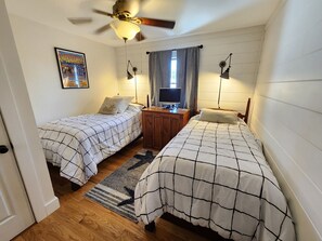 A bedroom with two beds, a ceiling fan, a TV, and a wooden cabinet. - Pony Tales | Near Assateague & Wildlife Refuge (Chincoteague Island)