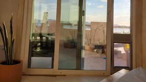 Et værelse med en stor skydedør, der fører ud til en udendørs terrasse med krukkeplanter og udsigt over landskabet.