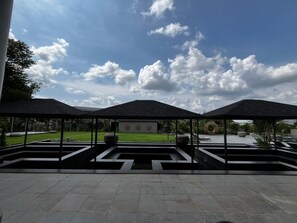 A covered outdoor area with a geometric design, a grassy lawn, and a clear sky.