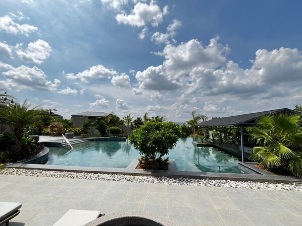 A swimming pool with a clear sky, surrounded by greenery and a covered area.