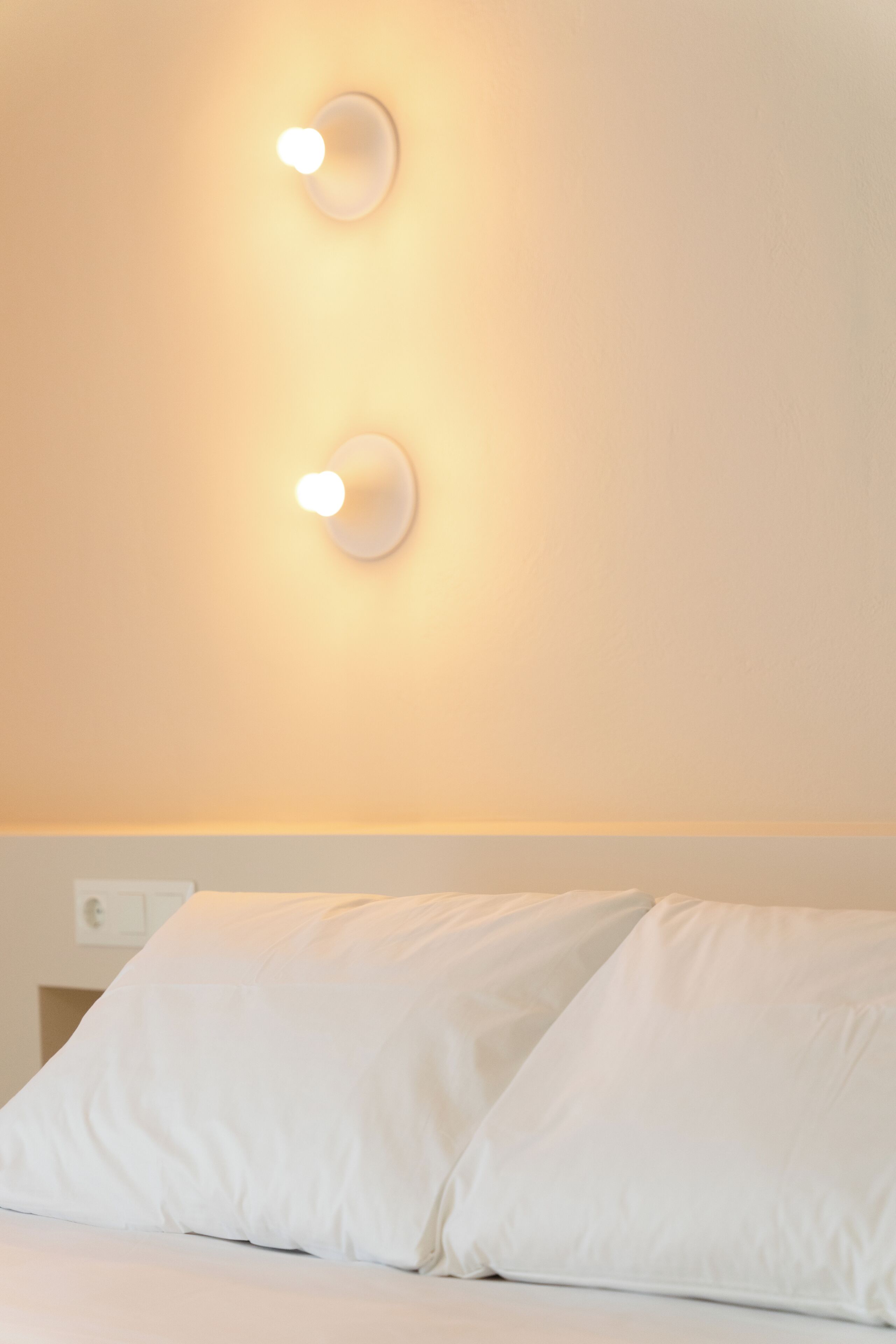 A hotel room with two white pillows and a wall-mounted light fixture.