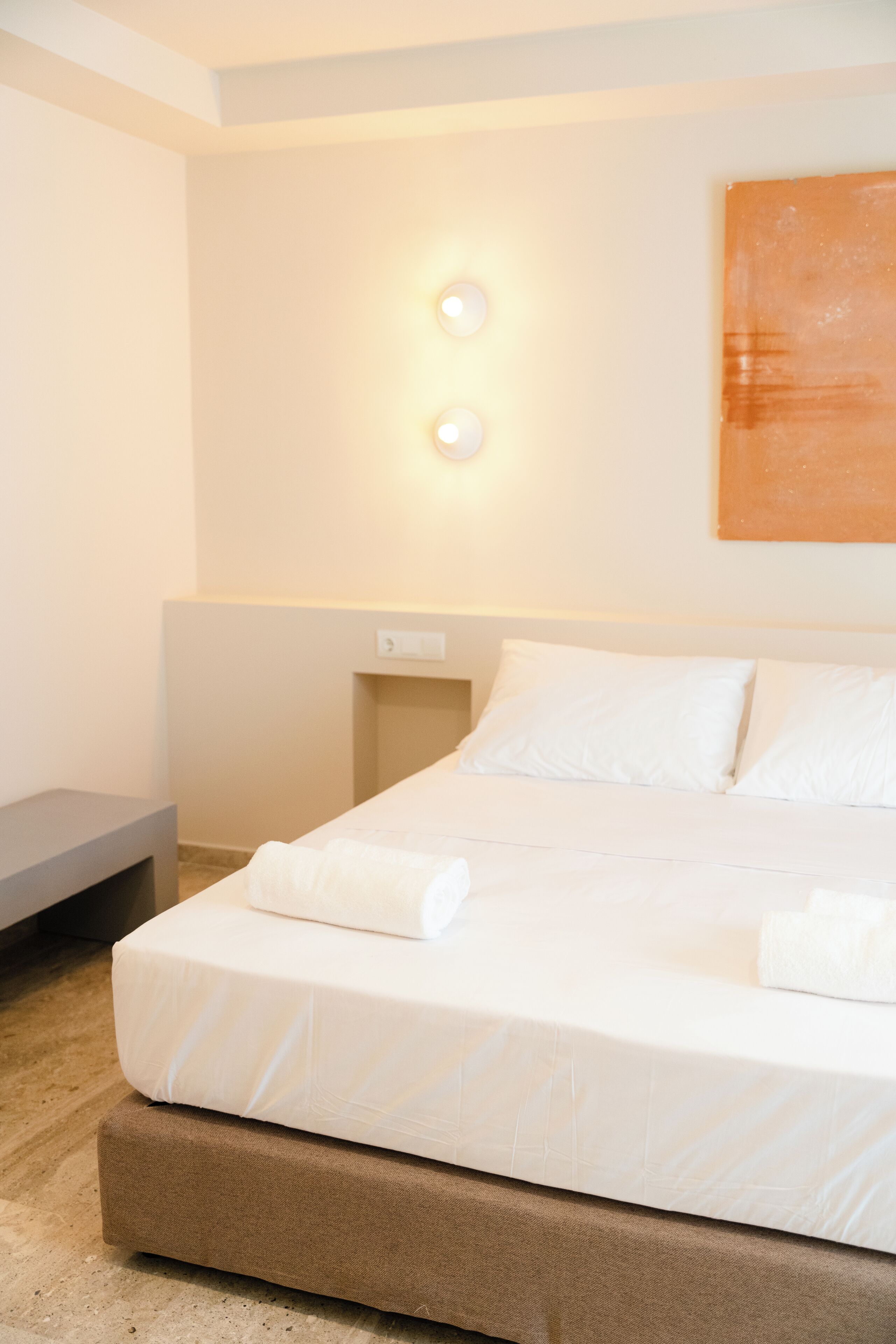 A neatly made bed with white linens, a bedside table, and a wall-mounted light fixture.