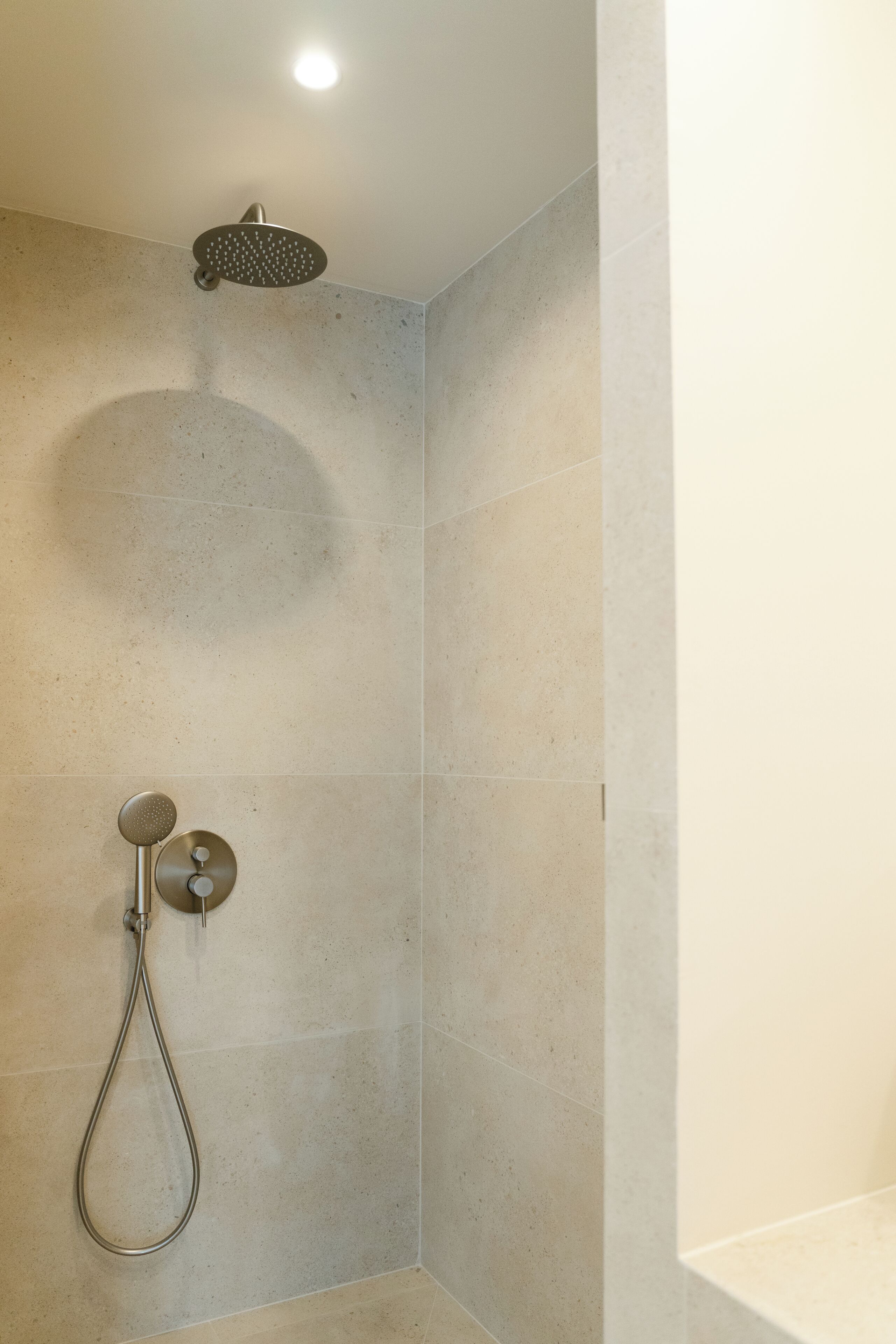 A shower area with a handheld showerhead and a wall-mounted control.