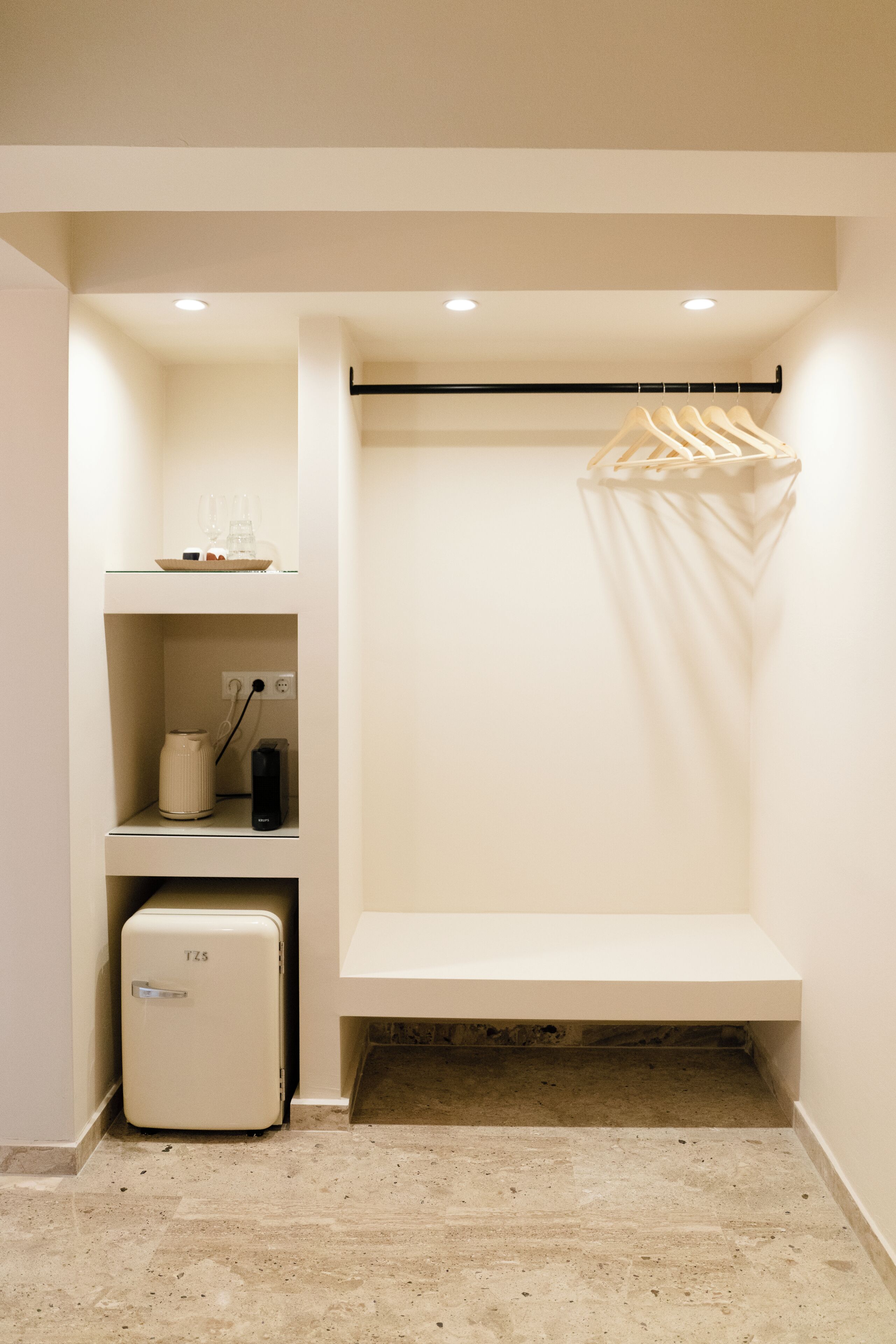 Un closet pequeño con espacio para entrar, que incluye un refrigerador empotrado, un estante con un recipiente de vidrio y una barra para colgar ropa.