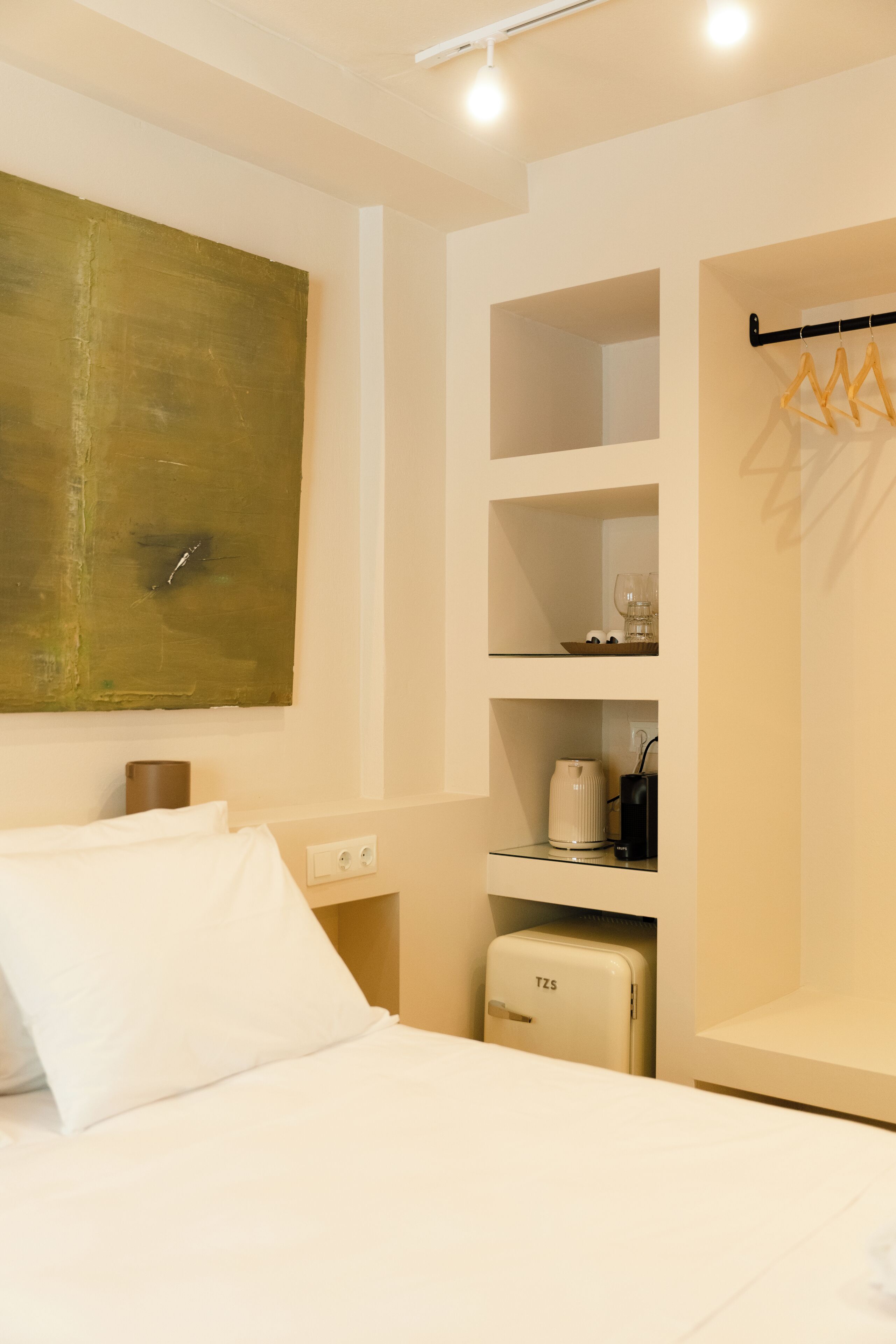 Hotelkamer met een bed, een koffieapparaat, een minibar, een kapstok en een groot abstract schilderij aan de muur.