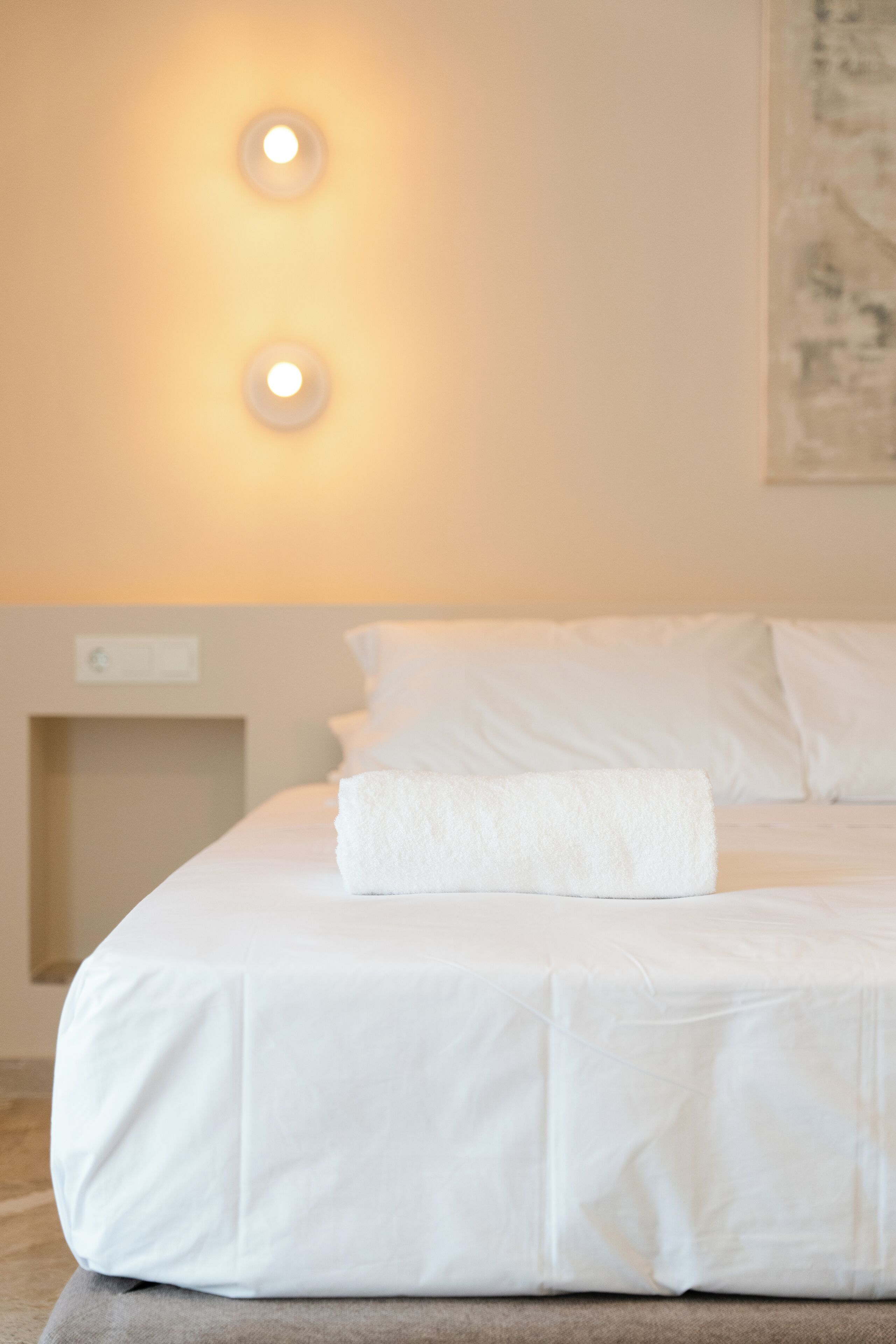 Un lit bien fait, avec une couette blanche et une serviette blanche pliée.