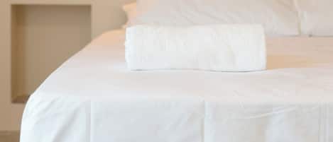 A neatly made bed with a white duvet and a folded white towel.