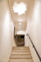 Una escalera con barandilla, una lámpara arriba y una puerta al final.