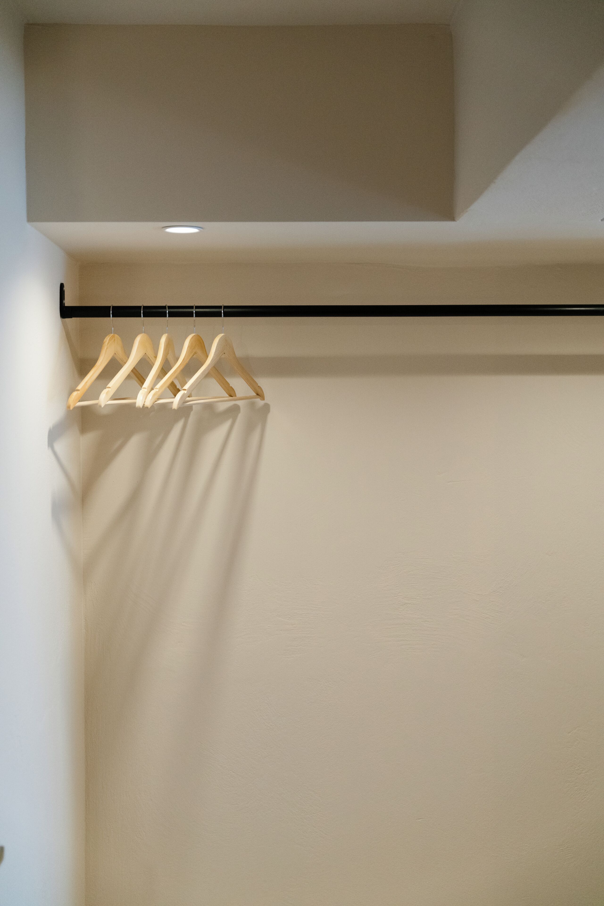 Quarto com parede branca, teto preto e um cabideiro de madeira com cabides.