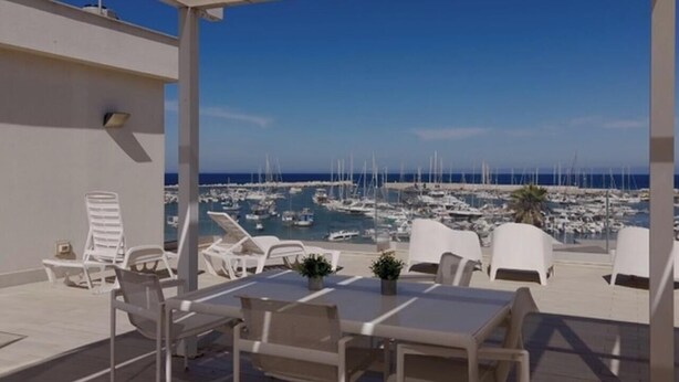 Een terras met uitzicht op een jachthaven, witte lounge fauteuils en een tafel met potplanten.