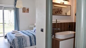 Een slaapkamer met een bed, nachtkastje, gordijnen en uitzicht op de omgeving.