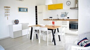 Een moderne keuken met witte en gele kastjes, een eettafel met stoelen en een witte bank.