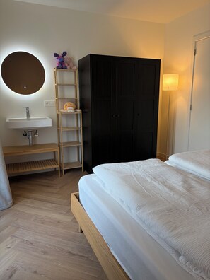 Ein Schlafzimmer mit einem Bett, einem Holzschrank, einem runden Spiegel über einem Waschbecken und einem Regal mit Stofftieren.