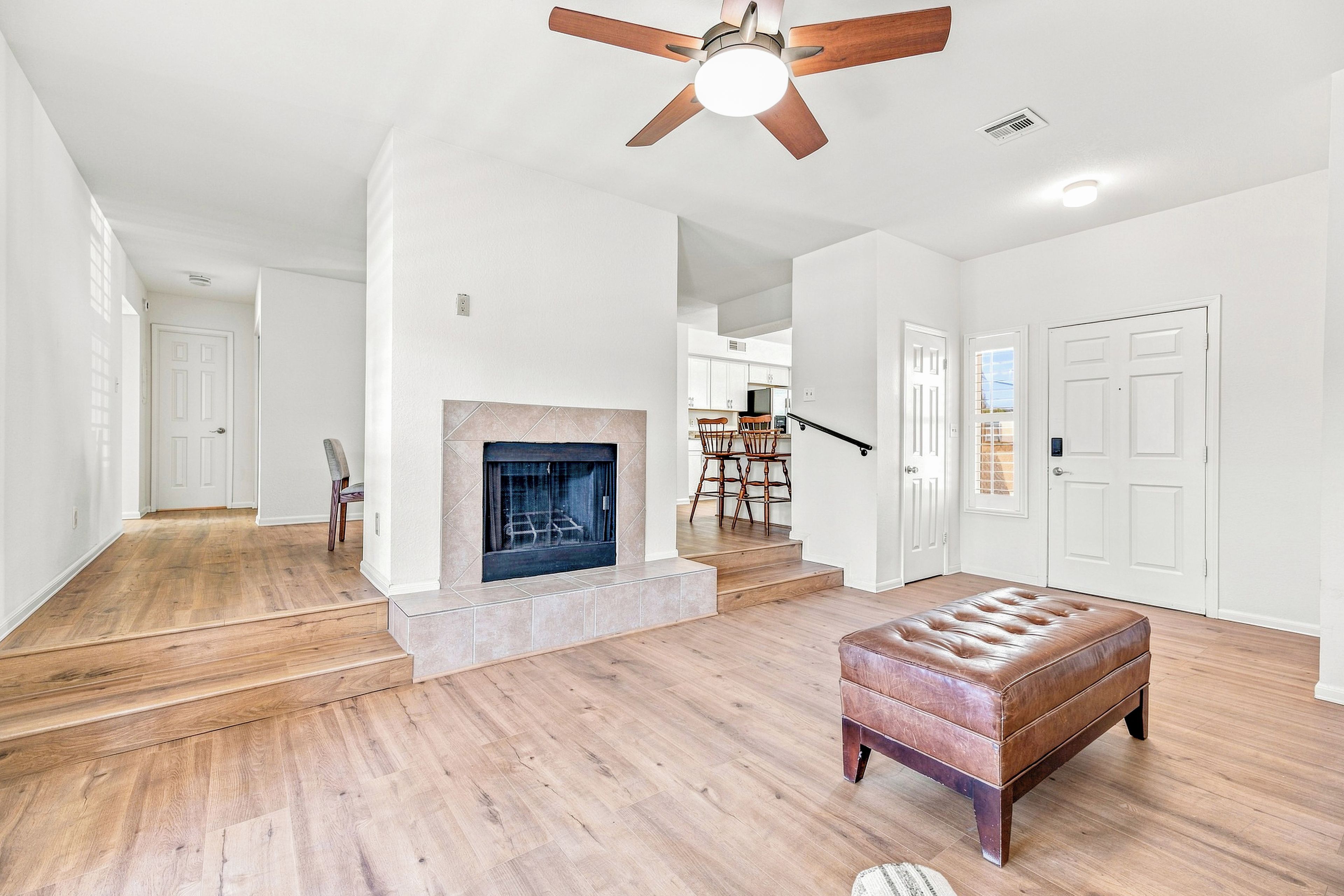 A spacious living room with hardwood flooring, a fireplace, a ceiling fan, and a large window.