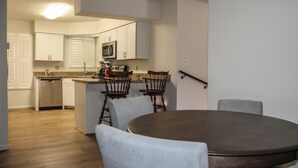 Una cocina moderna con armarios blancos, un microondas y un lavavajillas. Hay una zona de comedor con una mesa redonda y cuatro sillas.