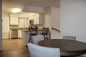 Cozinha moderna com armários brancos, micro-ondas e lava-louças. Há um espaço de refeições com uma mesa redonda e quatro cadeiras.