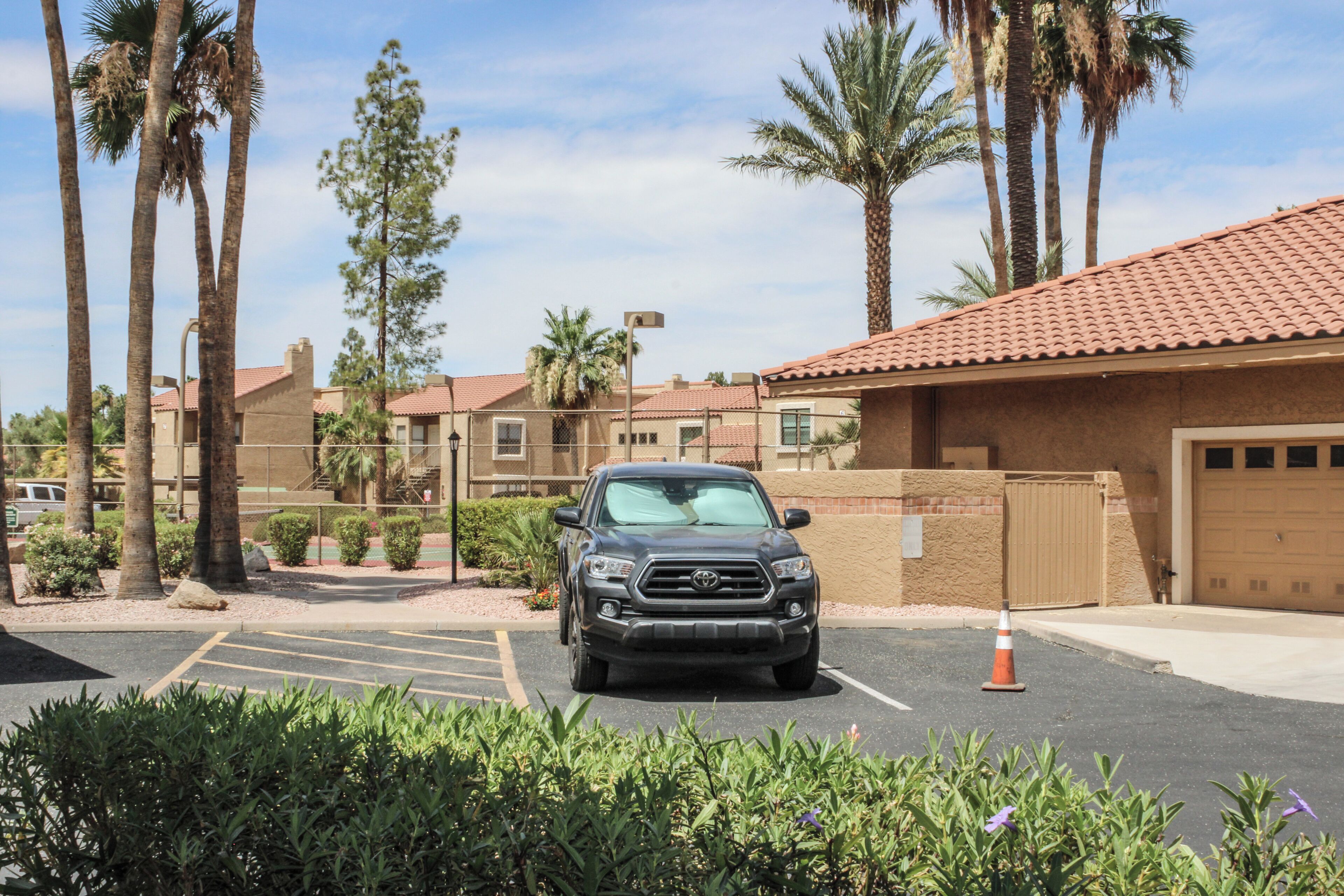 A parking lot with a vehicle, palm trees, and a building with a red-tiled roof.