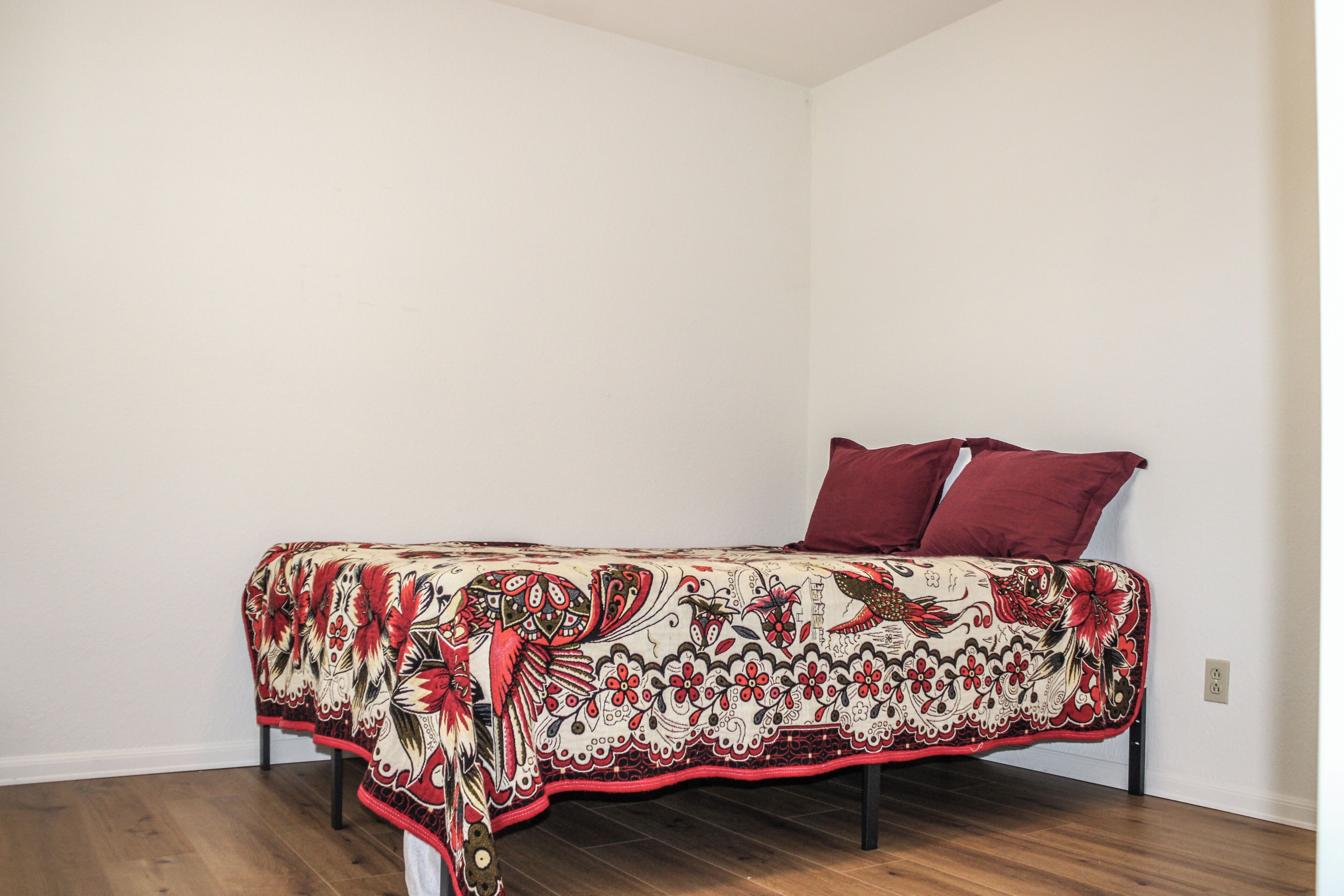 Ein Einzelbett mit gestreiftem Überwurf und zwei Kissen in einem Zimmer mit weißen Wänden und Holzboden.