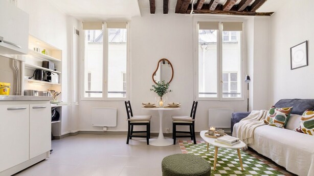 A compact living space with a kitchenette, dining area, and a sofa with patterned cushions. - FurtiveStay - Sentier - Ste Foy - 1BDR 4P (Paris)