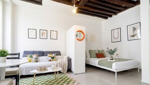 A modern living room with a sofa, a bed, a dining table, and a checkered rug. - FurtiveStay - Sentier - Ste Foy - 1BDR 4P (Paris)