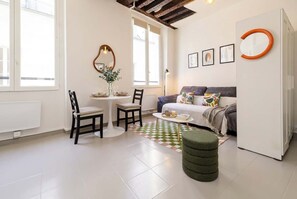 Ein modernes Wohnzimmer mit einer Couch, einem Esstisch mit Stühlen, einem Couchtisch und einem grünen Hocker.