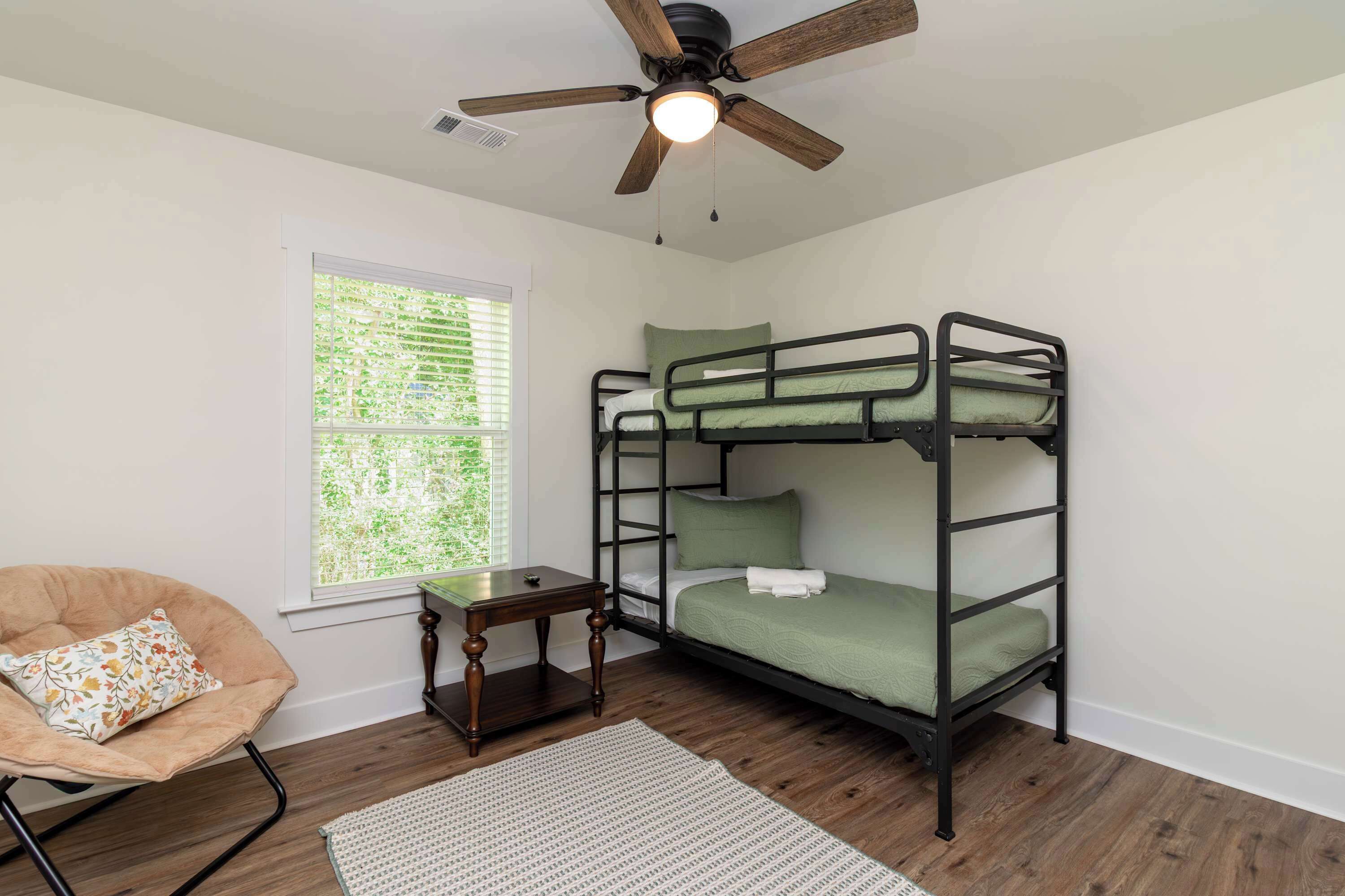 Une chambre avec un lit superposé, un ventilateur de plafond, une petite table, une chaise et une fenêtre avec des stores.