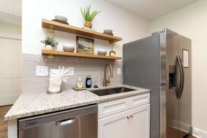 Eine Küche mit Edelstahl-Kühlschrank, Geschirrspüler, einer Arbeitsplatte aus Granit und Holzregalen mit Dekoration.