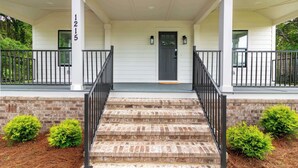 A front porch with steps leading to a door, a mailbox, and a brick wall. - The Magnolia on 54th (Columbus)