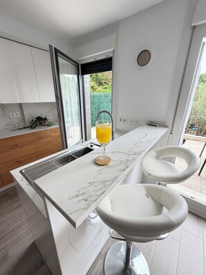 A modern kitchen with a marble countertop, two white bar stools, and a glass of orange juice.