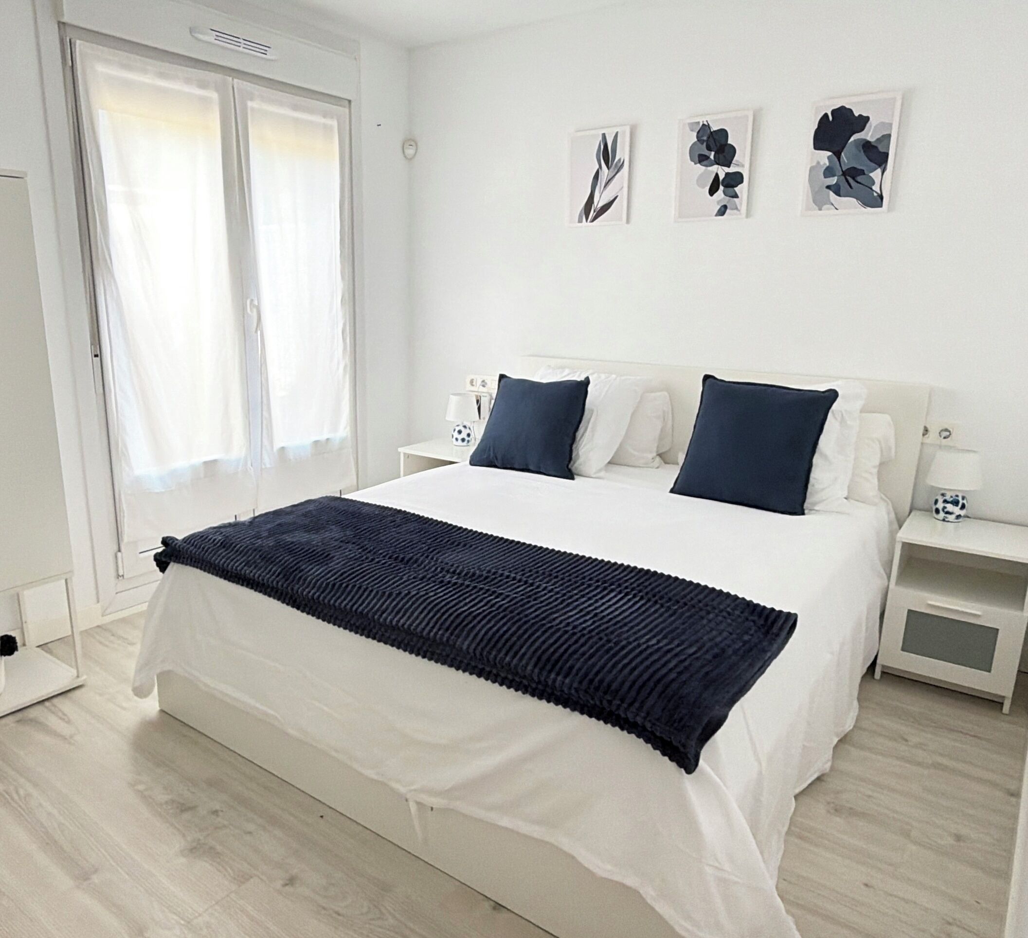 Een slaapkamer met een bed, twee nachtkastjes, een raam met gordijnen en wanddecoratie.